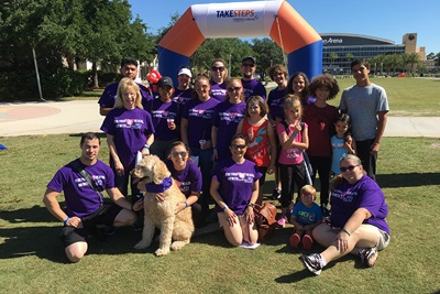 A group of people wearing matching purple shirts take a photo at the finish line of an event